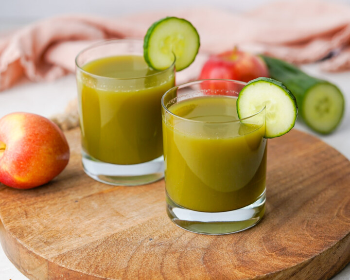 two cups of cucumber apple juice with sliced cucumbers for garnish