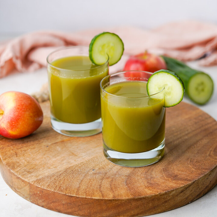 two cups of cucumber apple juice with sliced cucumbers for garnish