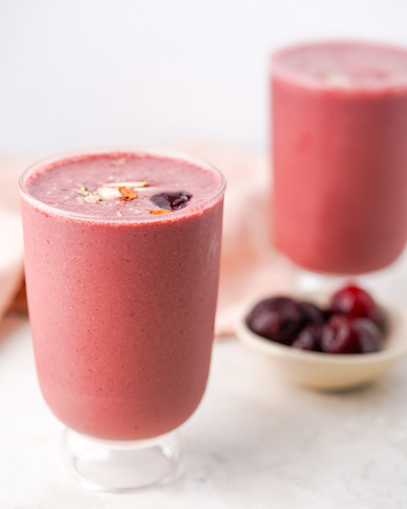 two cups filled with cherry smoothie with pitted cherries in a small bowl