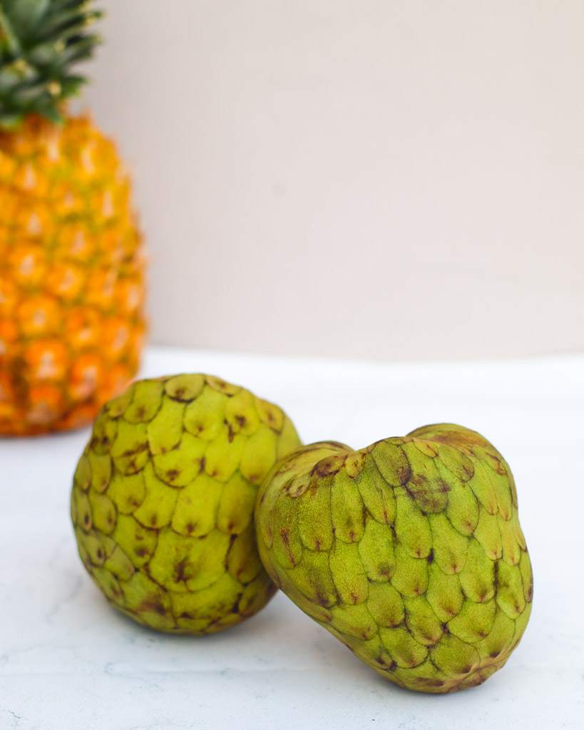 two cherimoya fruits with a pineapple in the background