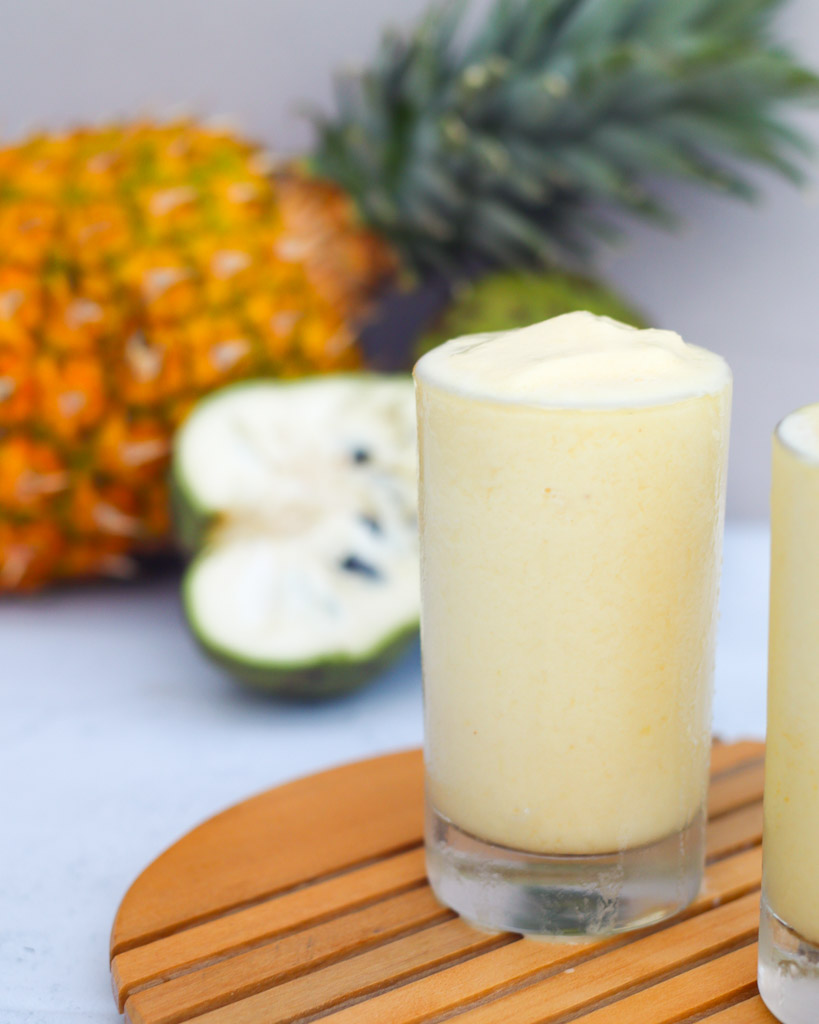 a glass full of cherimoya smoothie with fruits in the background