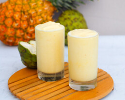 two glasses full of cherimoya smoothie with fruits in the background