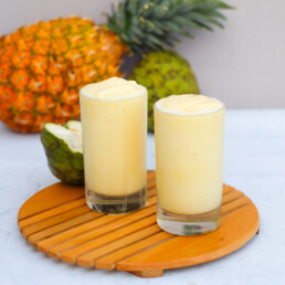 two glasses full of cherimoya smoothie with fruits in the background