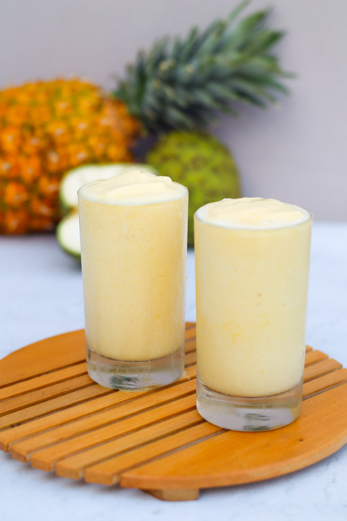 two glasses full of cherimoya smoothie with fruits in the background
