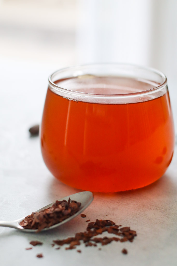 a clear mug filled with cacao tea with a spoon and scattered cacao nibs