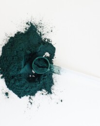 green spirulina powder on a white background with a measuring teaspoon filled with spirulina in the powder