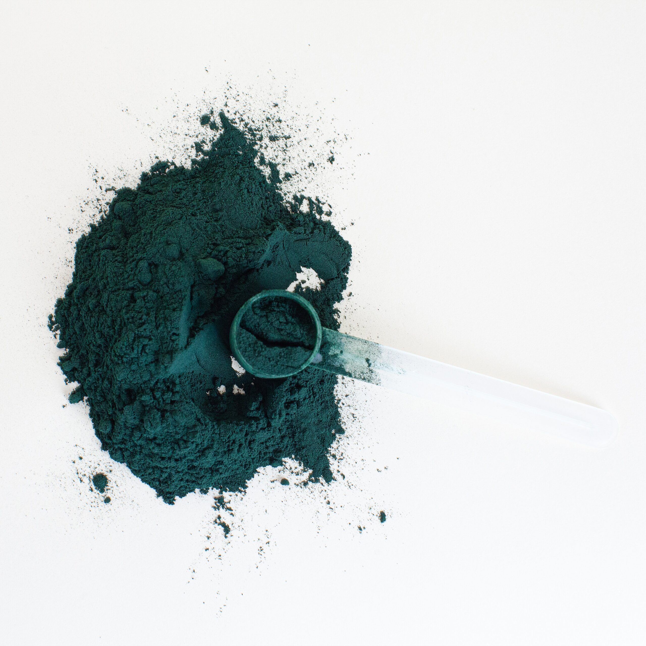 green spirulina powder on a white background with a measuring teaspoon filled with spirulina in the powder