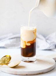 a pitcher pouring milk into a glass with espresso