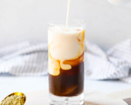 a pitcher pouring milk into a glass with espresso