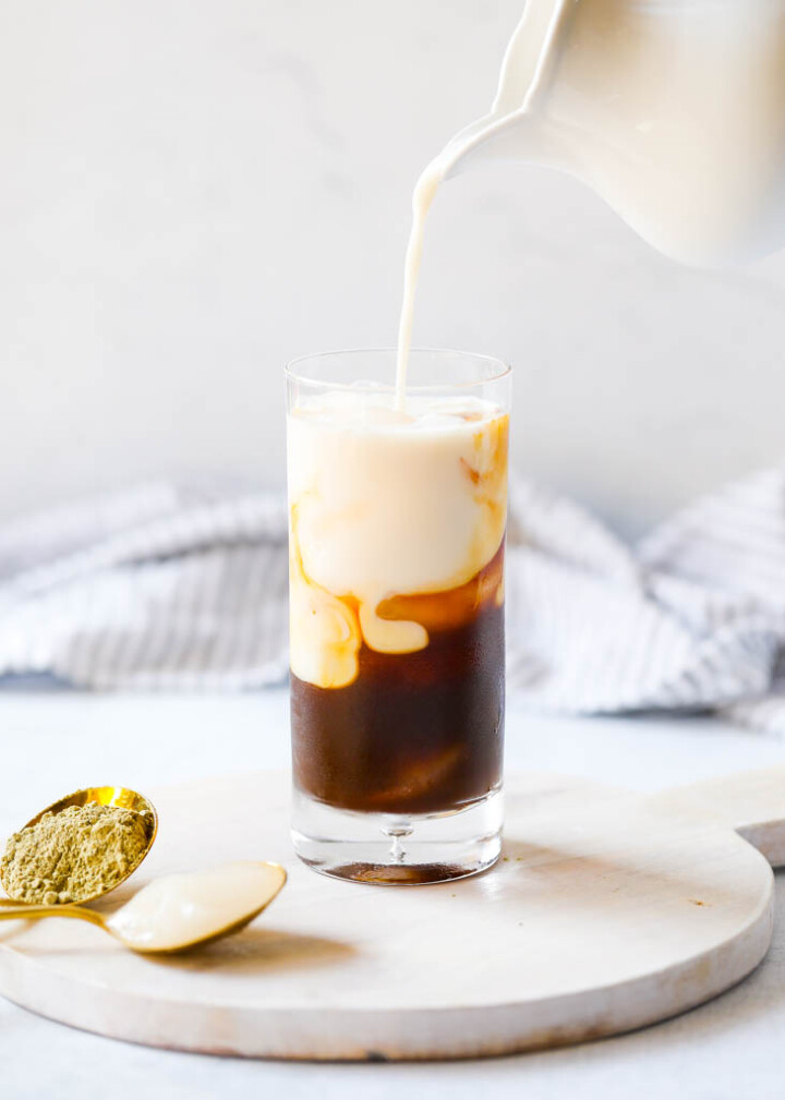 a pitcher pouring milk into a glass with espresso